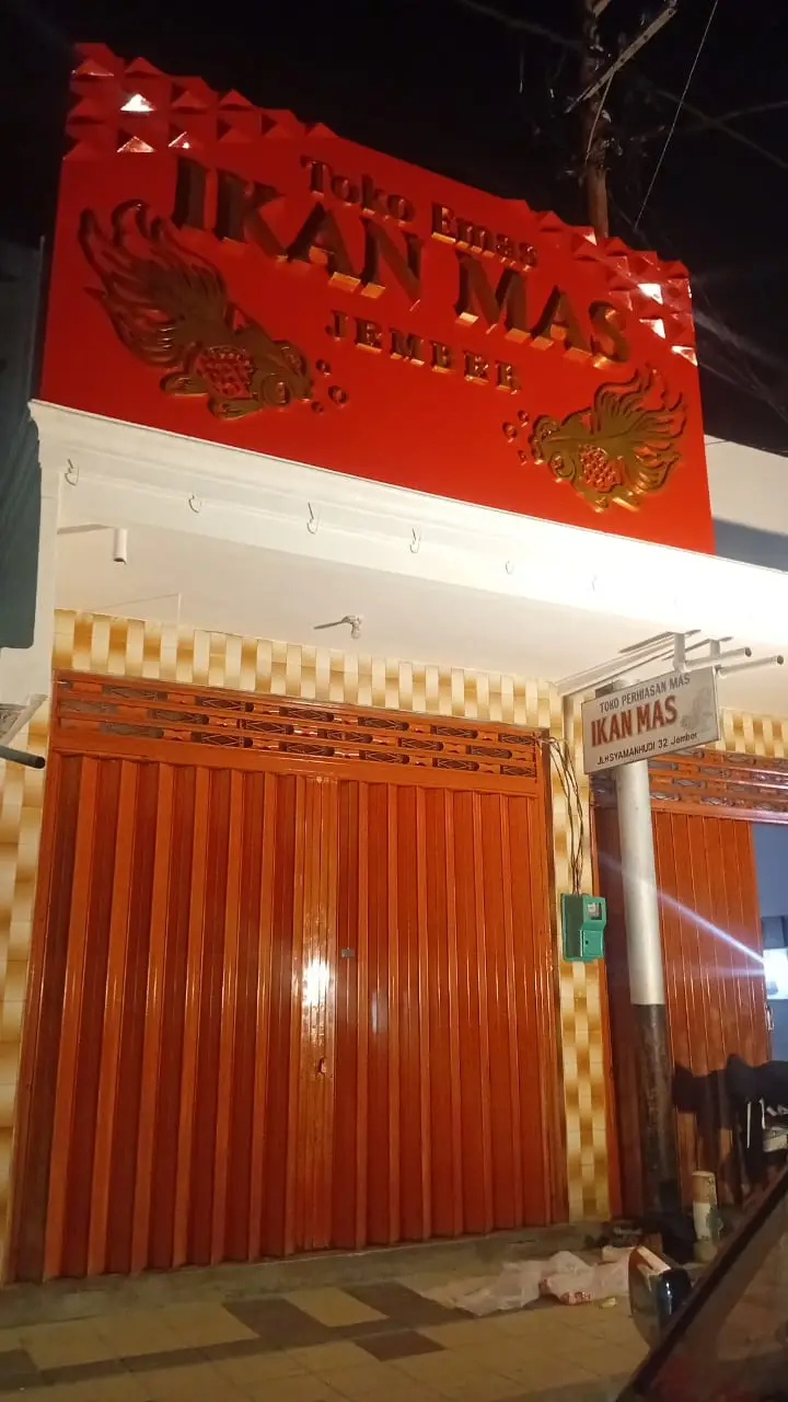 Papan nama huruf timbul Toko Emas Ikan Mas Jember saat menyala di malam hari